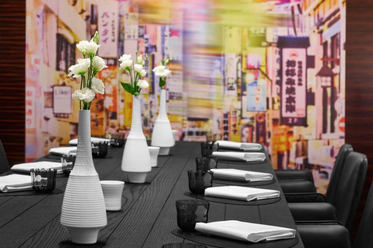 Detaiaufnahme des Schimkow.TISCH, das ist eine lange schwarz geflämmte Tafel in der L.A. Jordan Lounge, an der Genussmenschen zusammen kommen und Wein und Kulinarik genießen. Im Hintergrund des neonfarbene Graffiti mit den Letten "L. A. Jordan"